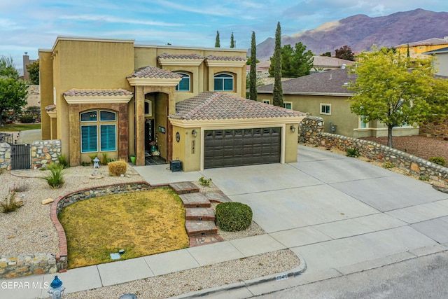 mediterranean / spanish-style home with a tile roof, stucco siding, an attached garage, a mountain view, and driveway