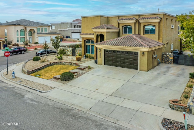 mediterranean / spanish house featuring a garage, a tile roof, concrete driveway, a gate, and stucco siding