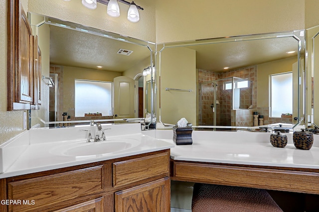 full bath featuring visible vents, a shower stall, vanity, a textured wall, and a textured ceiling