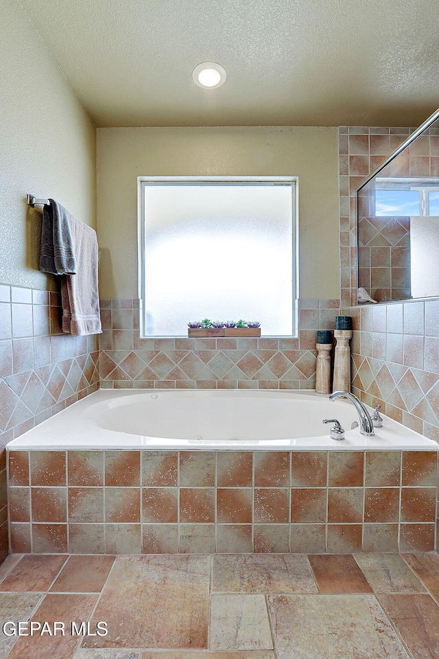 bathroom with a textured ceiling, tile walls, and a bath