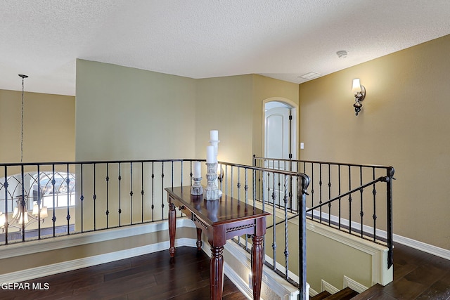 hall featuring visible vents, an upstairs landing, hardwood / wood-style flooring, a textured ceiling, and baseboards