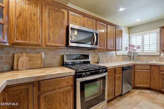 kitchen featuring backsplash, a textured ceiling, stainless steel appliances, and tile counters