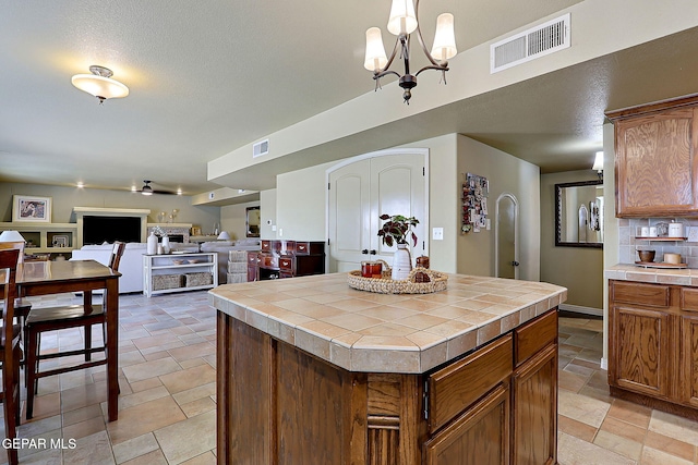 kitchen featuring tile countertops, visible vents, stone tile floors, and decorative backsplash