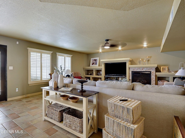 living area featuring a glass covered fireplace, baseboards, a textured ceiling, and ceiling fan