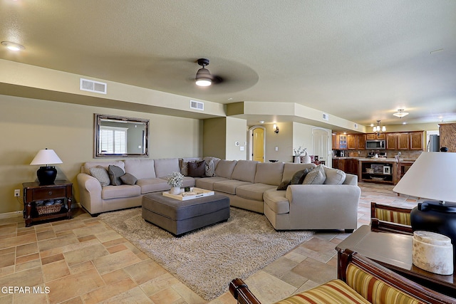 living room with stone tile floors, visible vents, a textured ceiling, and ceiling fan