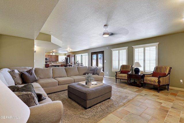 living area with stone finish flooring, baseboards, a textured ceiling, and ceiling fan