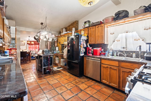 kitchen with brown cabinetry, lofted ceiling, appliances with stainless steel finishes, tile patterned floors, and a sink