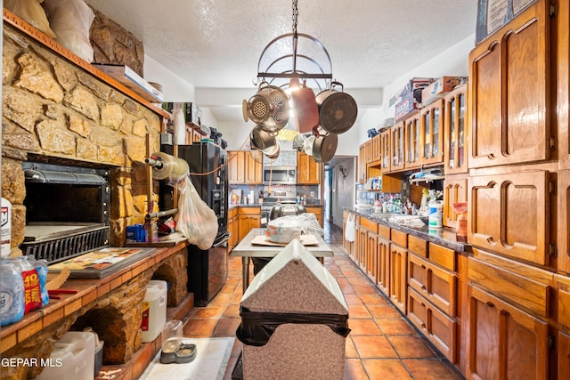 kitchen with a textured ceiling, light tile patterned floors, appliances with stainless steel finishes, brown cabinets, and tasteful backsplash