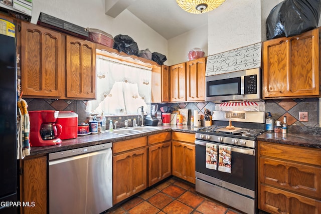 kitchen with appliances with stainless steel finishes, brown cabinetry, a sink, and backsplash