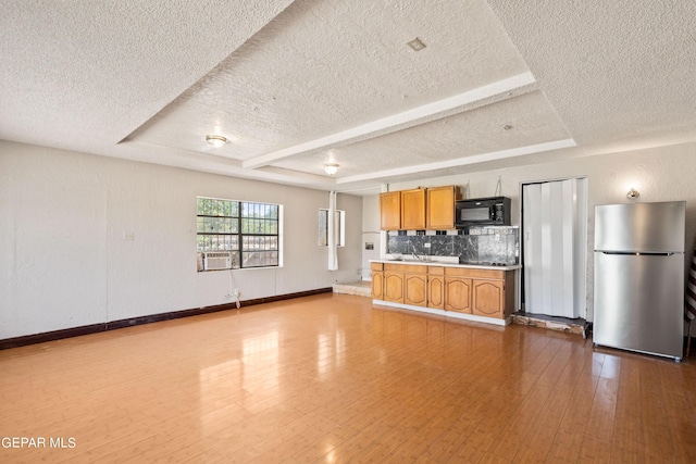 kitchen featuring black microwave, dark wood-style flooring, a tray ceiling, and freestanding refrigerator