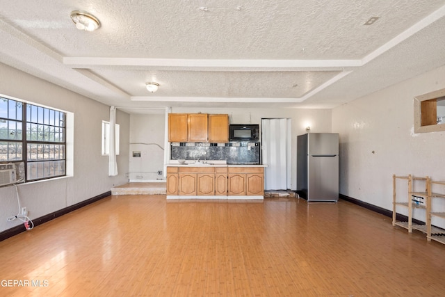 kitchen with brown cabinetry, freestanding refrigerator, a textured ceiling, black microwave, and baseboards