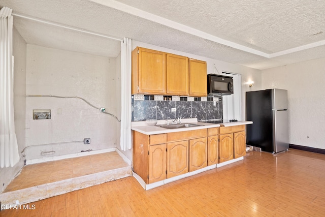 kitchen with black microwave, a sink, light wood-style floors, light countertops, and freestanding refrigerator