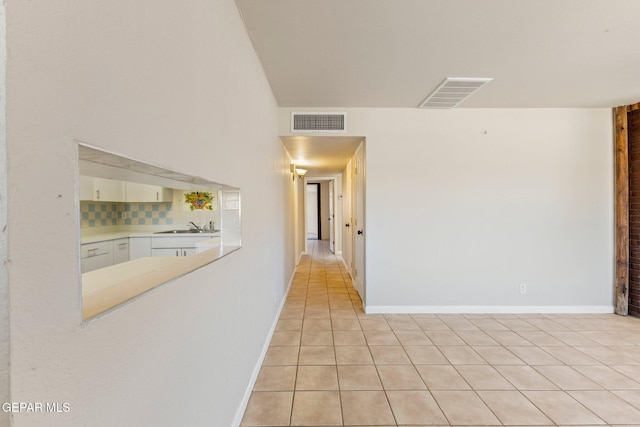 corridor featuring light tile patterned floors, visible vents, baseboards, and a sink