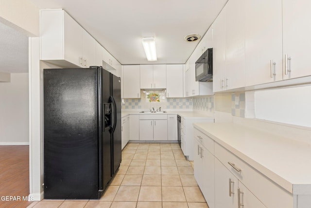 kitchen featuring tasteful backsplash, light countertops, light tile patterned floors, white cabinets, and black appliances