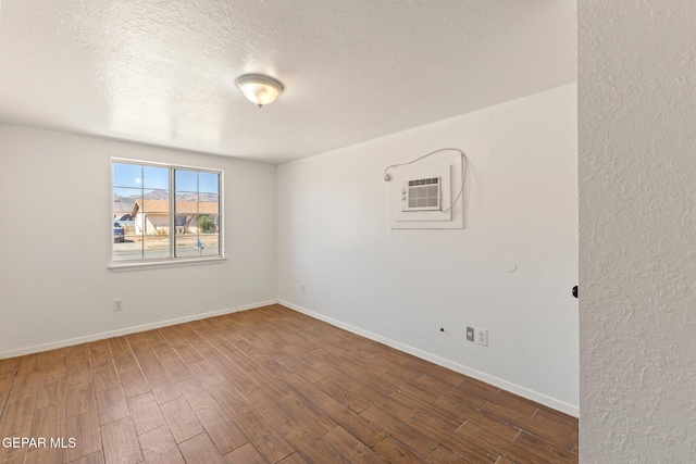 empty room with baseboards, a textured ceiling, wood finished floors, and a wall unit AC