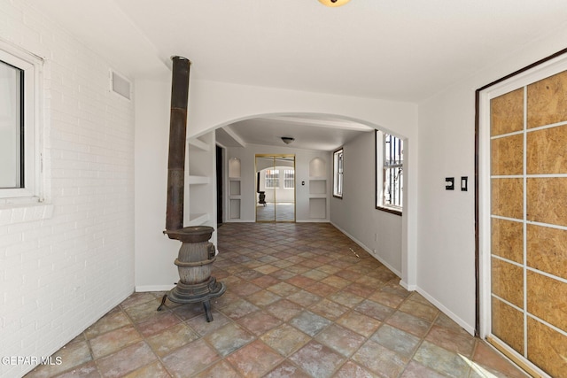 hall featuring visible vents, brick wall, baseboards, arched walkways, and stone finish floor