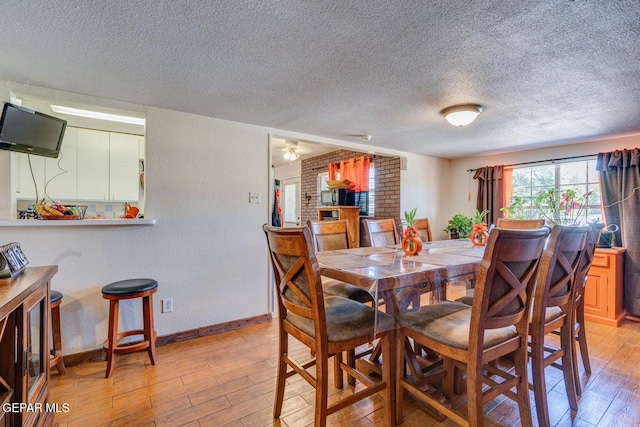 dining room featuring light wood finished floors, a textured ceiling, baseboards, and a textured wall