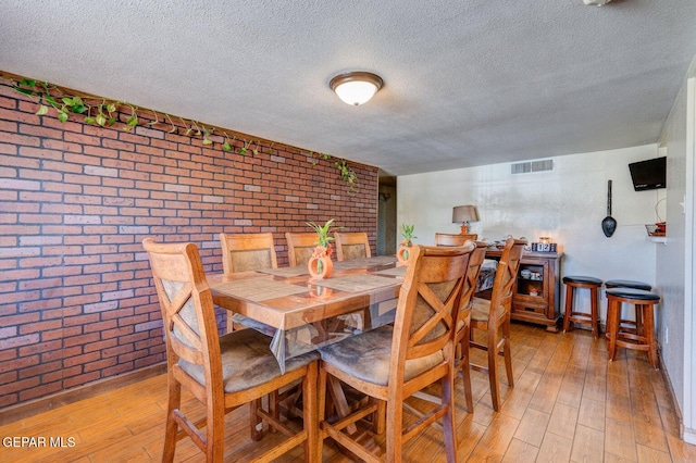 dining area featuring visible vents, a textured ceiling, brick wall, and light wood finished floors