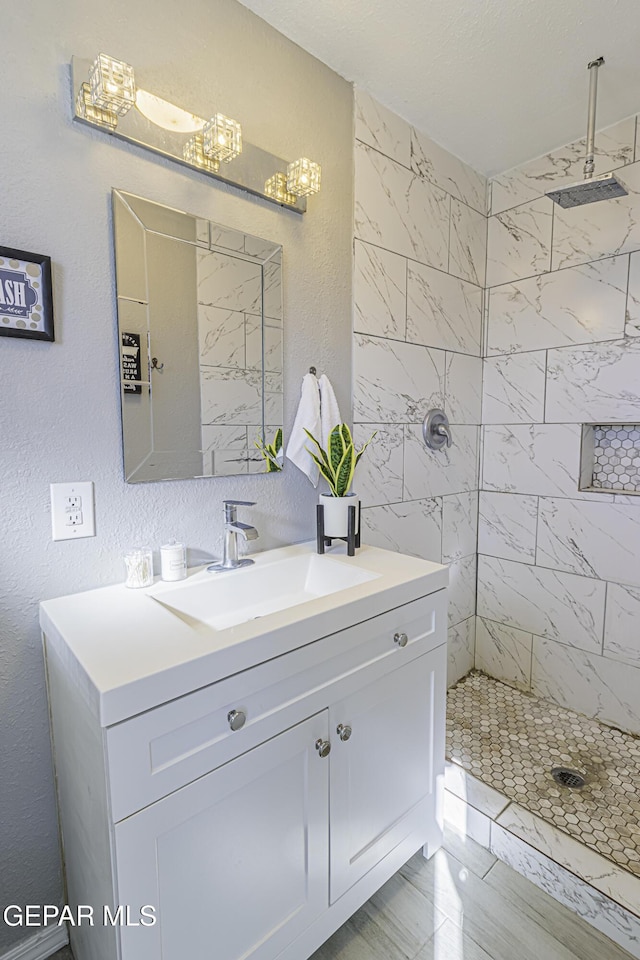 full bathroom with a textured wall, marble finish floor, a tile shower, and vanity