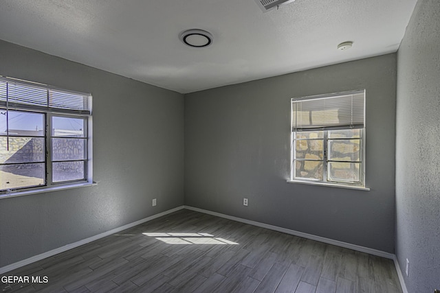 unfurnished room featuring a textured wall, baseboards, and wood finished floors