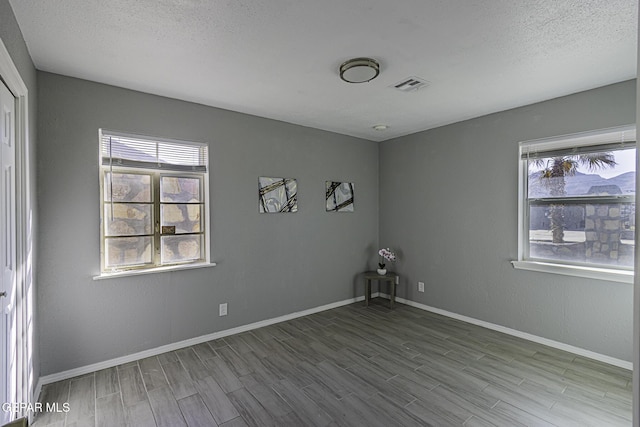 unfurnished room with baseboards, visible vents, a wealth of natural light, and wood finished floors