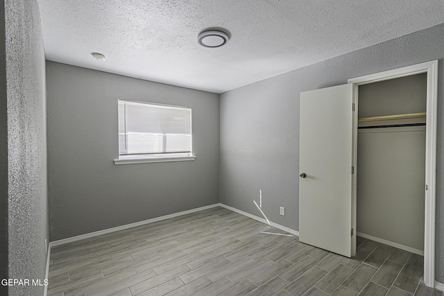 unfurnished bedroom featuring baseboards, a textured wall, wood finished floors, a textured ceiling, and a closet