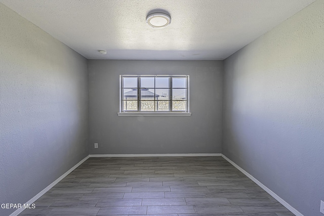 unfurnished room featuring a textured wall, a textured ceiling, baseboards, and wood finished floors