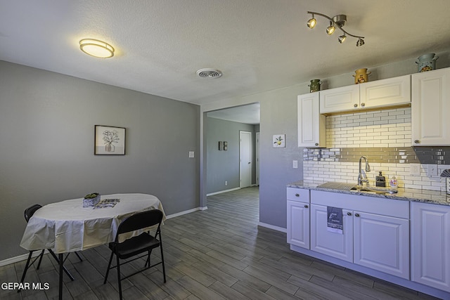 kitchen featuring dark wood-style flooring, a sink, visible vents, white cabinets, and decorative backsplash