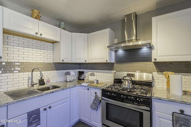 kitchen featuring decorative backsplash, white cabinets, wall chimney exhaust hood, stainless steel gas range, and a sink