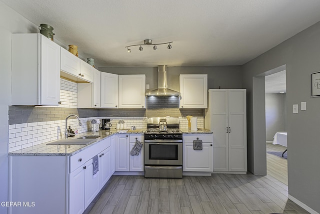 kitchen with backsplash, white cabinets, a sink, wall chimney range hood, and stainless steel gas range oven