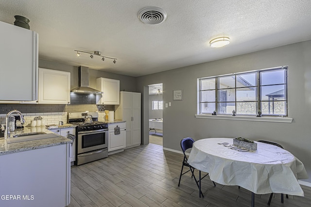 kitchen with a sink, visible vents, backsplash, wall chimney exhaust hood, and gas range