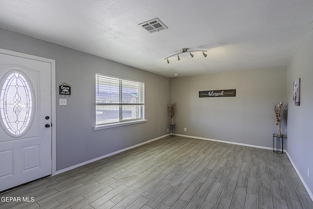 foyer entrance with a textured ceiling, wood finished floors, visible vents, and baseboards