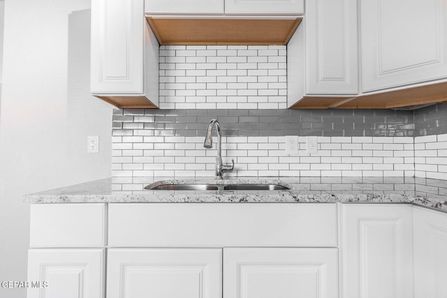 kitchen with tasteful backsplash, a sink, light stone counters, and white cabinets