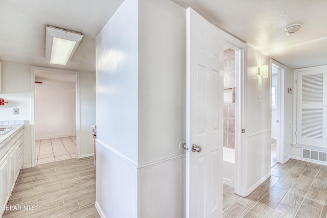 hall featuring baseboards, visible vents, and wood finish floors