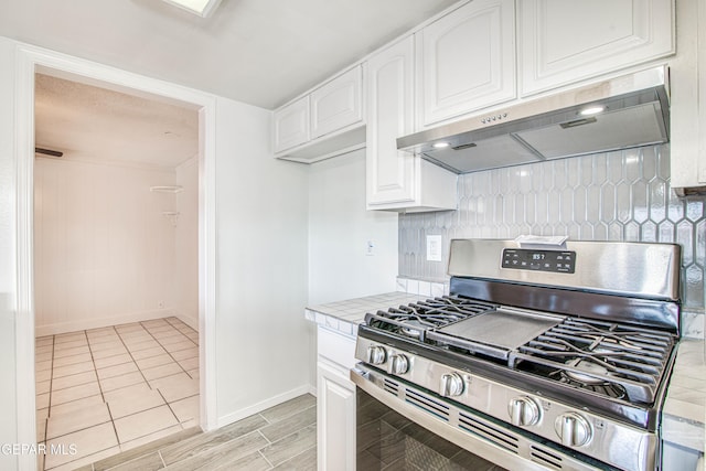 kitchen featuring light countertops, backsplash, stainless steel gas stove, white cabinetry, and ventilation hood