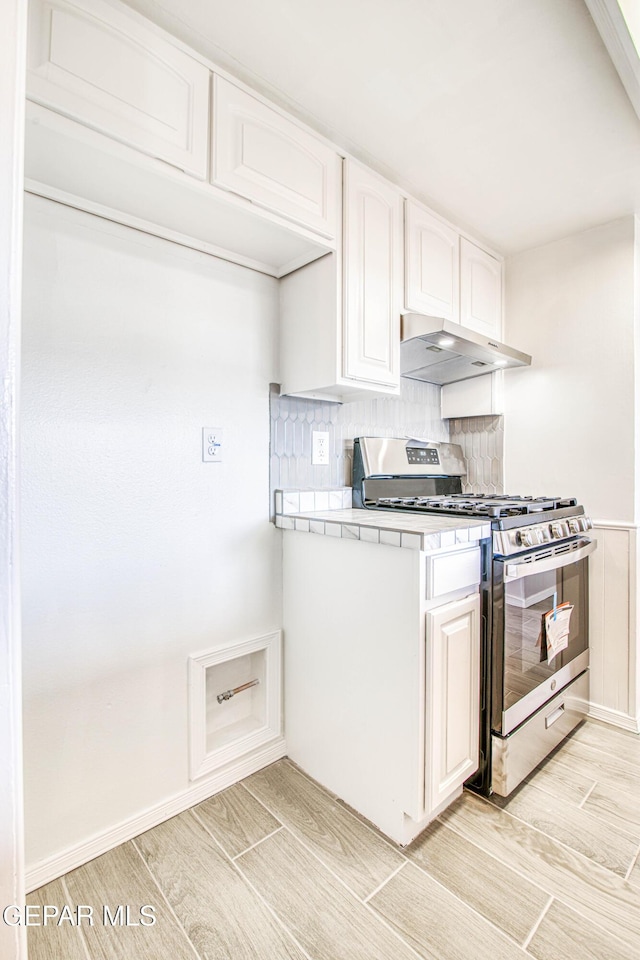 kitchen with light countertops, wood tiled floor, white cabinets, stainless steel gas range, and under cabinet range hood