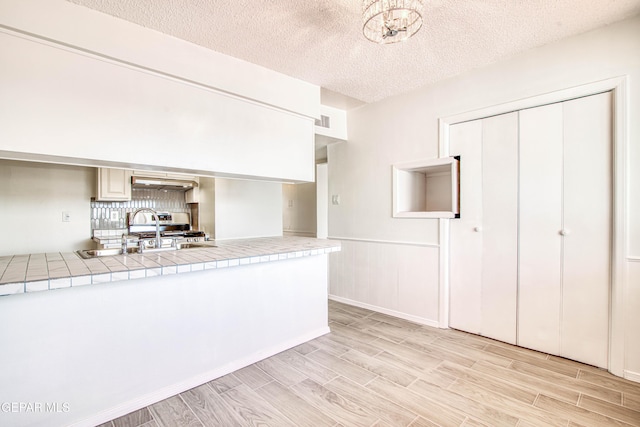 kitchen featuring visible vents, tile countertops, wood tiled floor, a textured ceiling, and a sink