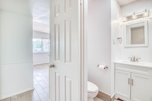 bathroom featuring wood finish floors, vanity, toilet, and a textured ceiling