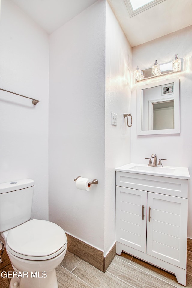 half bath featuring toilet, visible vents, baseboards, vanity, and wood tiled floor