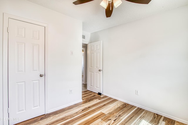 unfurnished bedroom with a textured ceiling, ceiling fan, light wood-style flooring, and baseboards