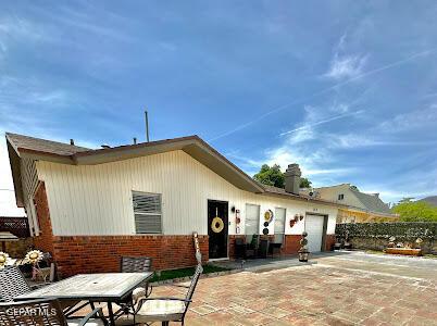 rear view of property featuring outdoor dining space, a patio, a garage, decorative driveway, and brick siding