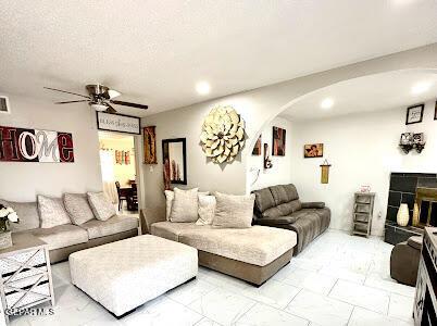 living room with ceiling fan, arched walkways, recessed lighting, a fireplace with raised hearth, and marble finish flooring
