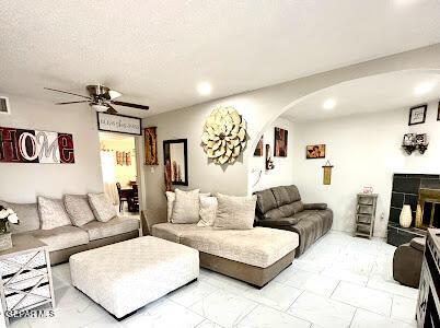 living area with arched walkways, marble finish floor, a textured ceiling, and ceiling fan