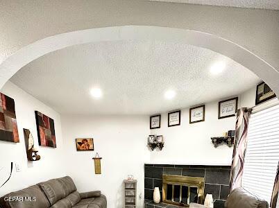 living area with arched walkways, a fireplace, and a textured ceiling