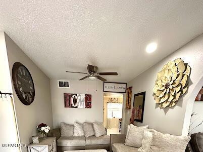 living area featuring visible vents, a textured ceiling, and a ceiling fan