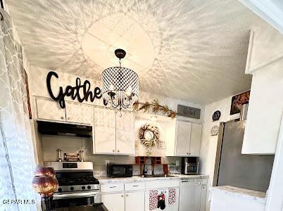 kitchen with light countertops, white cabinets, appliances with stainless steel finishes, under cabinet range hood, and a chandelier