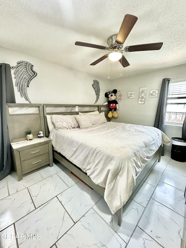 bedroom with a textured ceiling, marble finish floor, and ceiling fan