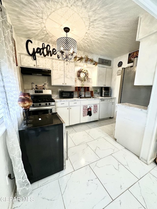 kitchen with white cabinets, under cabinet range hood, appliances with stainless steel finishes, marble finish floor, and a chandelier