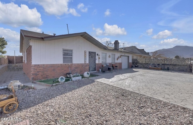 exterior space with driveway, fence, an attached garage, brick siding, and a patio area