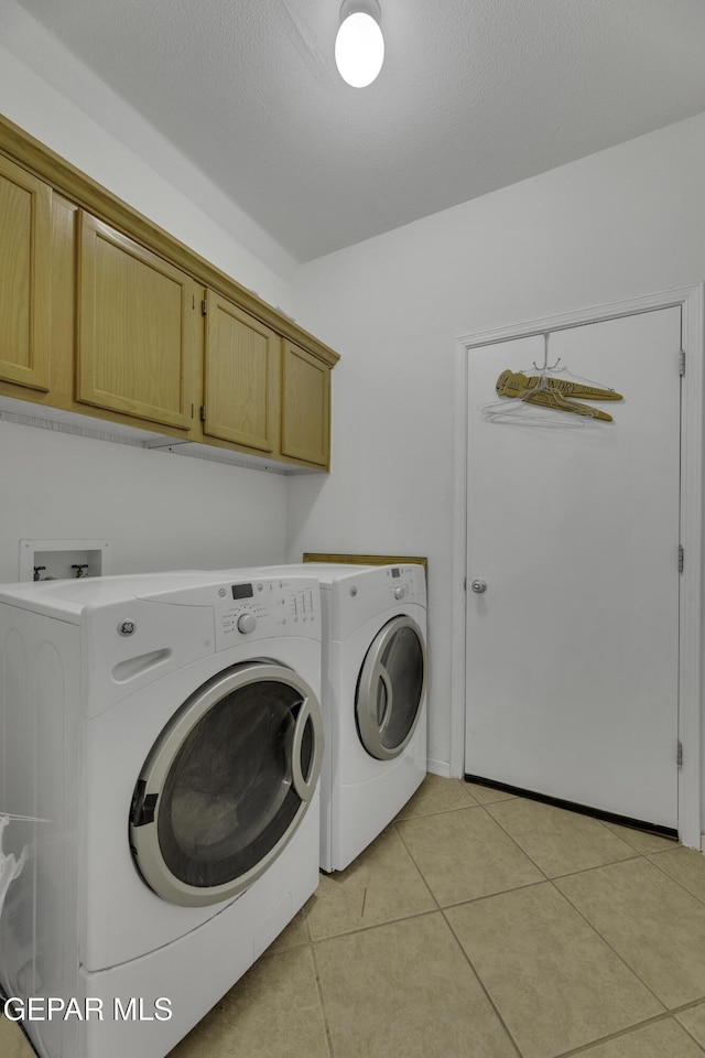 laundry area featuring light tile patterned floors, cabinet space, separate washer and dryer, and a textured ceiling